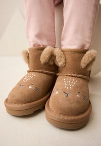 Bottes bottines en suède marron pour tout-petit avec motif visage de lapin, comprenant des détails brodés et des accents doux en fourrure pour les oreilles. Semelle en caoutchouc plate.
