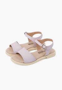 Lilac sandals featuring two wide straps, adjustable ankle strap with buckle, tan insole, and flat light-colored sole.