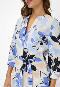 Abito a fiori in tessuto leggero, con tonalità di blu e beige, scollo a v, chiusura con bottoni e dettaglio in vita legato.
