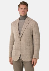 Beige geruite blazer met een enkele knoop, twee voorzakken en ingesneden revers, gedragen over een grijze coltrui.
