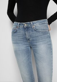 Vaqueros de denim azul claro con diseño de pierna recta, que presentan bolsillos frontales, cierre de botón y un ligero desgastado para un aspecto texturizado.