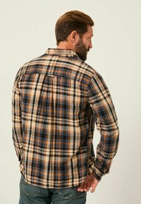 Flanellhemd mit einem Karo-Muster in Blau, Orange und Creme. Verfügt über eine Schulterpasse und knöpfbare Manschetten. Hergestellt aus weichem Stoff.