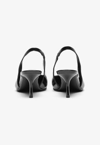 Fekete, magas sarkú cipők fényes, lakkbőr felülettel, nyitott háttal és körülbelül 3 hüvelyk magas, vékony sarkakkal.