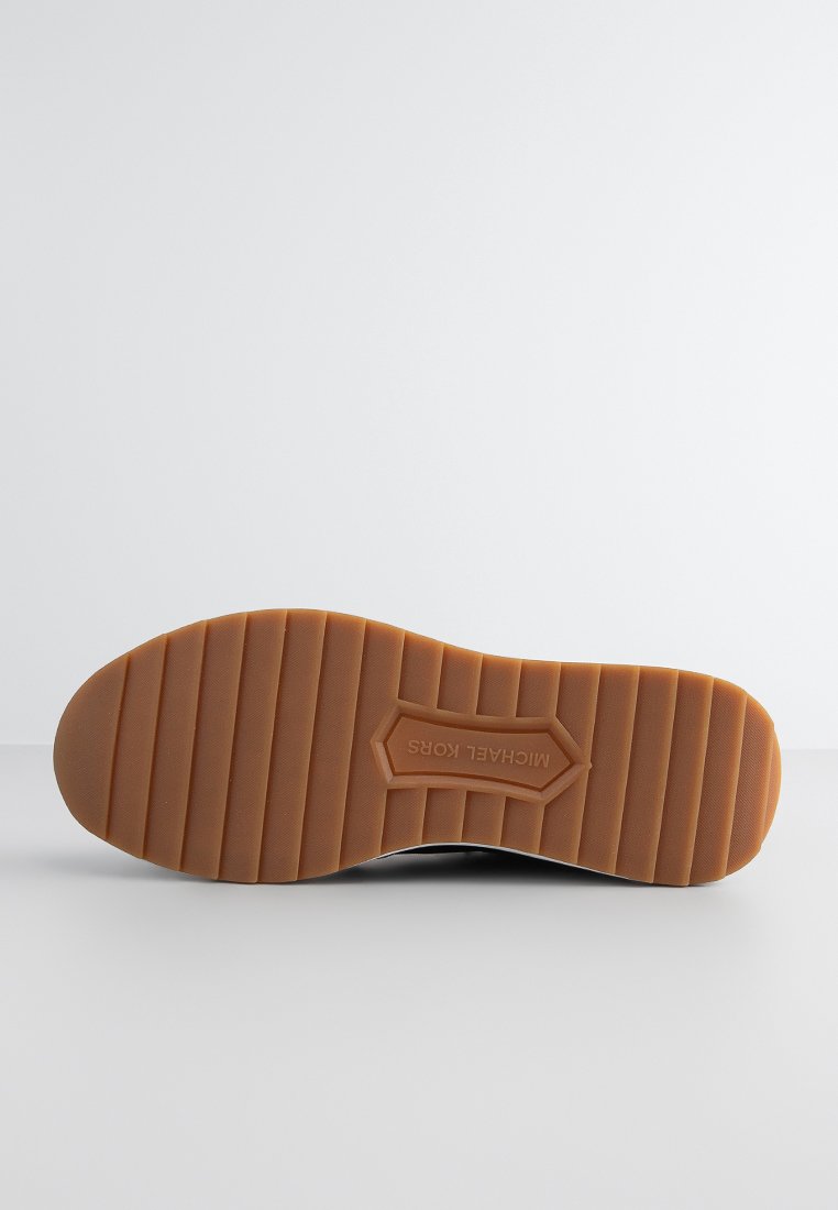 Semelle de chaussure avec une surface texturée et rainurée en caoutchouc marron clair. Présente le nom de la marque embossé "MICHAEL KORS" en accent central.