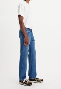T-shirt bianco a maniche corte, jeans blu in denim a gamba dritta e sneakers nere con accenti arancioni e beige. Design semplice, vestibilità classica.