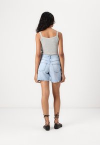Top gris sin mangas combinado con pantalones cortos de mezclilla azul claro. Características notables: diseño ajustado, bolsillos traseros y zapatos negros con cordones.