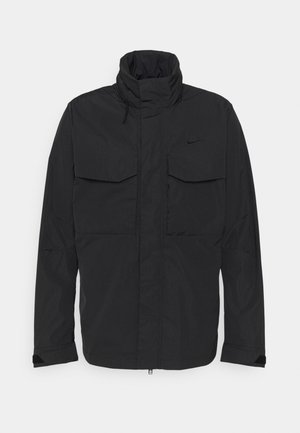 Black Nike jacket with high collar, front zipper, flap chest pockets, and adjustable sleeve cuffs.