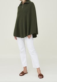 Maglione oversize verde oliva con collo a zip, lavorazione a maglia strutturata, abbinato a pantaloni bianchi a gamba dritta e sandali bassi marroni.