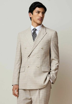 Light-colored double-breasted suit with a textured fabric, featuring a checked pattern, well-defined lapels, and two buttons on the front.