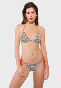 Čierno-biely vzorovaný bikiny s červenými detailmi. Vrchná časť má trojuholníkové košíčky a nastaviteľné ramienka; spodná časť má viazacie bočné detaily.
