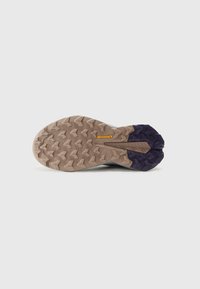 Semelle de chaussure de trail avec une surface en caoutchouc texturé, des sections marron et violet, et un motif de crampons en zigzag pour l'adhérence et la durabilité.