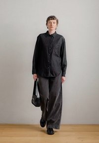 Μαύρο πουκάμισο με κουμπιά και τσέπη, συνδυασμένο με σκούρες γκρίζες φαρδιές παντελόνες και μαύρα παπούτσια. Το σύνολο ολοκληρώνεται με μια μαύρη τσάντα ώμου.