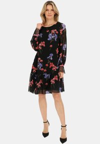 Czarna sukienka w kwiaty z długimi, przezroczystymi rękawami. Posiada czerwone i fioletowe wzory kwiatowe, falbaniasty dół oraz koronkowe wykończenia przy mankietach.