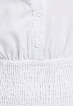 Hvid bluse med knaplukning foran, tekstureret smocket talje og korte ærmer. Materialet virker let og har en blød, glat tekstur.