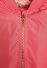 Primer plano de una chaqueta rosa con una cremallera dorada y cuello acanalado, mostrando un forro con estampado floral y una etiqueta de nombre dentro del cuello.