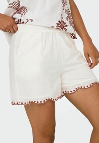 Shorts en lin blanc avec un ourlet festonné agrémenté de broderies bourgogne, dotés de poches latérales et d'une ceinture élastique.