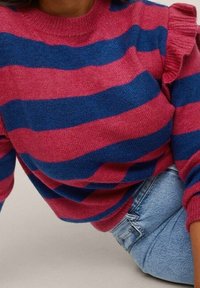 Gestreifter Pullover mit pinken und blauen horizontalen Streifen, ausgestattet mit einem gerippten Halsausschnitt und Rüschendetails an den Schultern, kombiniert mit Jeans.