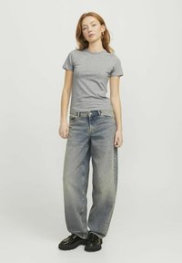 Grijze T-shirt met korte mouwen gecombineerd met losse lichtblauwe jeans. De outfit wordt compleet gemaakt met zwarte schoenen met een dikke zool.