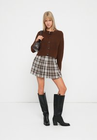 Rudas trumpas megztinis su juodais mygtukais, plaid mini sijonas smėlio ir rudos spalvos, juodi aukšti batai su kvadratiniais kulnais.
