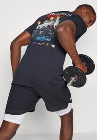 Black graphic t-shirt featuring a colorful monster truck design and text on the back, paired with dark shorts and white compression layers.