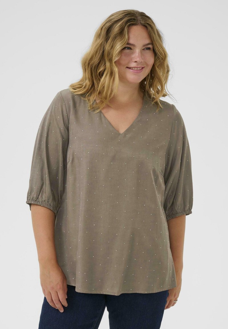 Top color marrón claro con escote en forma de V y mangas cortas abullonadas. Presenta pequeños puntos reflectantes y un diseño suelto y fluido.
