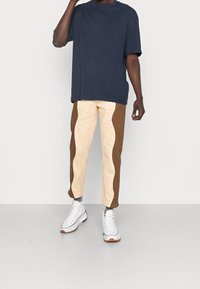 Mörkblå t-shirt med kort ärm kombinerad med byxor i krämfärg och bruna block. Vita sneakers har texturerade sulor och snörning.