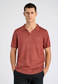 Kortärmad polo t-shirt i en dämpad röd färg, med V-ringad krage och ribbad nederkant. Tillverkad av ett mjukt, texturerat tyg.