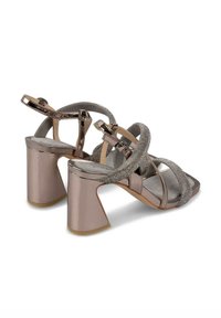 Sandalias de tacón en rosa metálico con tiras brillantes. Presentan un tacón cuadrado y un diseño de punta abierta, mostrando una textura suave y un acabado brillante.