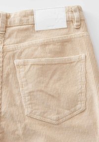Beige Cord-Hosen mit vertikaler Rippung, einer Gesäßtasche und einem weißen Patch-Label oberhalb des Bundes. Weicher Stoff mit maßgeschneidertem Schnitt.