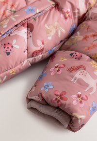 Ärmen på en rosa barnjacka med enhörningar, kaniner, nyckelpigor och färgglada blommor tryckta på vadderat tyg.