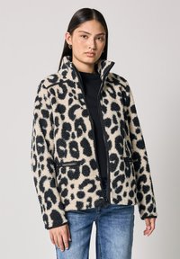 Chaqueta de forro polar con estampado de leopardo en crema y negro, con un alto cuello, bolsillos con cremallera y una tela suave y texturizada. Ajuste estructurado.