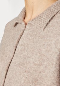 Collet et partie supérieure de la poitrine d'une personne portant un pull en laine doux de couleur beige clair avec un col côtelé.