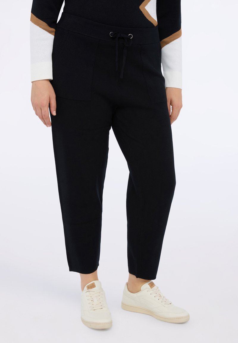 Granatowe spodnie dresowe z gumką w talii, dwoma przednimi kieszeniami i zwężanym krojem, połączone z białymi sneakersami dla casualowego wyglądu.