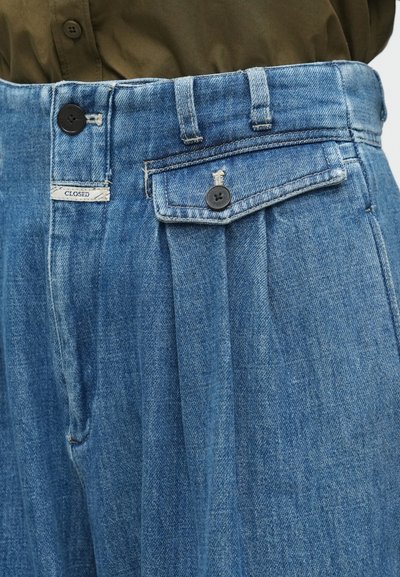 Τζιν παντελόνια με πιετά μπροστά, μπλε χρώμα, κλείσιμο με κουμπί και ετικέτα με την ένδειξη "CLOSED." Διακριτή υφή και κλασική γραμμή.
