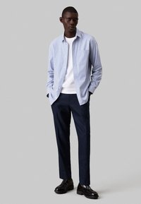 Camicia a righe blu chiaro e bianca con bottoni sopra una maglietta bianca, abbinata a pantaloni navy e mocassini neri. Vestibilità liscia e tailored.