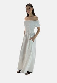 Hvid off-the-shoulder kjole med smocked liv, svævende bredbenet design og sidelommer. Letvægtsstof og glat tekstur.