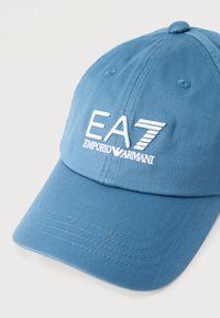 Plava baseball kapa od teksturiranog tkanina, s bijelim izvezenim logotipom "EA7 Emporio Armani" na prednjem dijelu. Dizajn s zakrivljenim obodom.