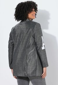 Silberner metallischer Blazer mit langen Ärmeln. Verfügt über einen weißen Akzent am Ärmel, eine glatte Textur und eine taillierte Form.