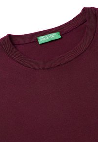 Bordeaux gebreide trui met een ronde halslijn en ribgebreide randen. Groen label met de tekst "United Colors of Benetton" zichtbaar op de kraag.
