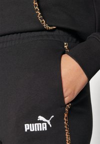 Calças de jogging pretas com um detalhe de estampa de leopardo ao longo do bolso. Apresenta um logo da Puma bordado em branco na perna. Tecido macio.