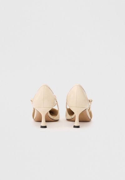 Μπεζ παλτό σκελετού ψηλοτάκουνα παπούτσια με αιχμηρή μύτη, ανοιχτές πλευρές και ελαφρώς κεκλιμένο τακούνι. Λείο υλικό με ελάχιστες λεπτομέρειες.