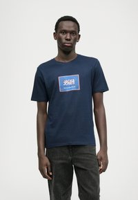 Námornícka modrá bavlnená tričko s vyšívanou štvorcovou nášivkou v červenej a bielej farbe. Krátke rukávy, okrúhly výstrih, uvoľnený strih, s textúrovanou látkou.