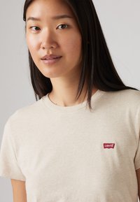 Beige bomull t-skjorte med korte ermer, med et lite rødt Levi's-logo-patch på brystet, glatt tekstur og klassisk rund hals-design.