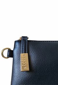 Borsa a mano in pelle nera con superficie strutturata, hardware in metallo dorato per la chiusura e un'etichetta decorativa dorata incisa con "Gaelle Paris."