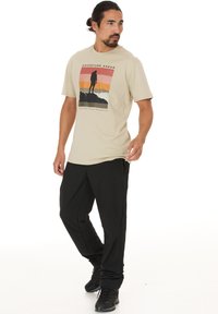 Beige puuvillane T-särk, millel on väligraafika, musta siluetti ja oranžikas-roosade triipudega. Kombineeritud mustade tõmblukuga pükste ja tumedate jalanõudega.