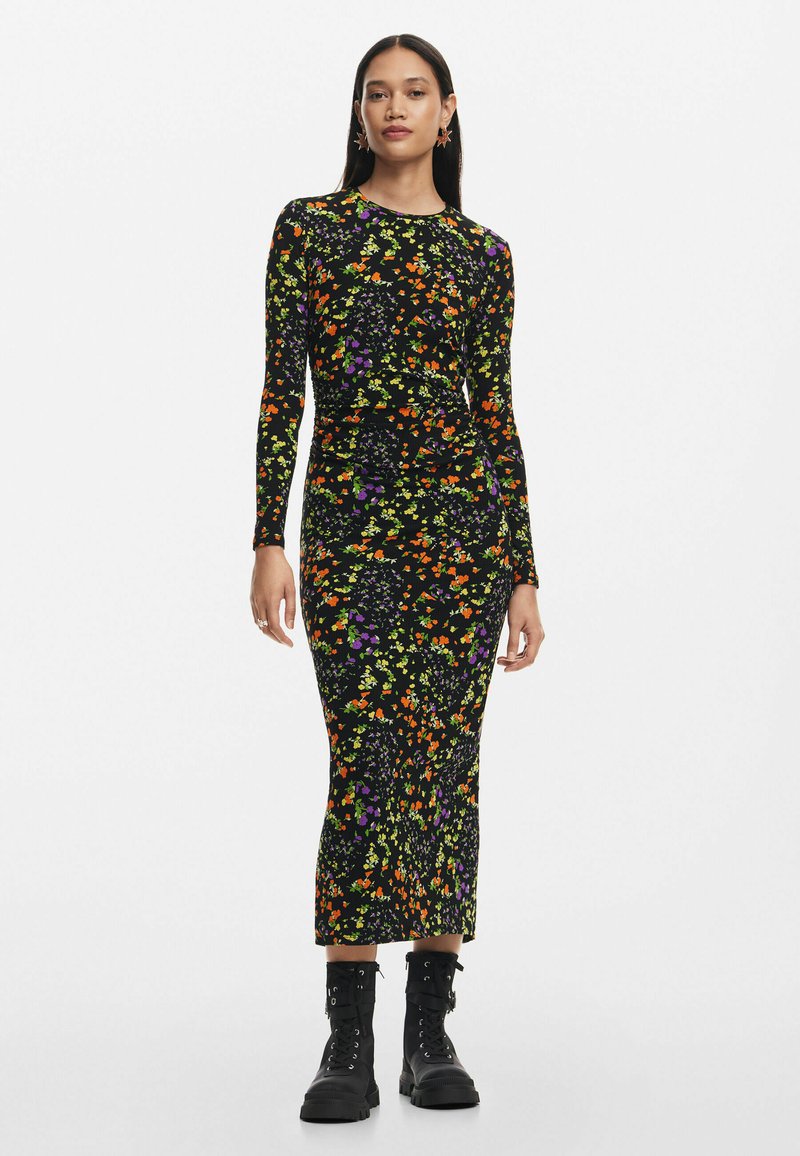 Hosszú ujjas fekete ruha színes virágmintával narancssárgában, lila és zöld színben. Feszes sziluett, térd alatt végződik, rugalmas anyagból készült, fekete csizmával párosítva.