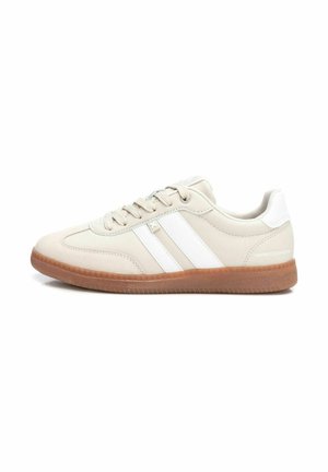 Zapatillas deportivas beige con rayas blancas, suela de goma, punta redondeada y cierre con cordones. Parte superior lisa y texturizada, diseño minimalista.