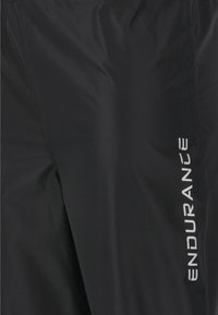 Zwarte sportbroek met een gladde, glanzende textuur, voorzien van een wit "ENDURANCE" logo aan de zijkant. Lichtgewicht, slim fit ontwerp geschikt voor sport.