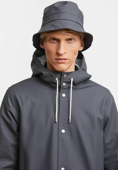 Grau wasserdichte Jacke mit Kapuze, ausgestattet mit silbernen Druckknöpfen und Kordelzügen. Kombiniert mit einem passenden grauen Bucket Hat.