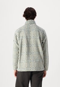 Fleece pullover met hoge kraag, met een geometrisch patroon in lichtgroen en beige. Zachte textuur; ruime pasvorm, lange mouwen.
